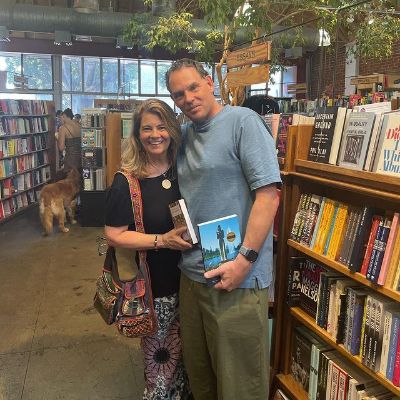 Both Lisa and Pete are in a library looking at the camera while holding books in their hand.